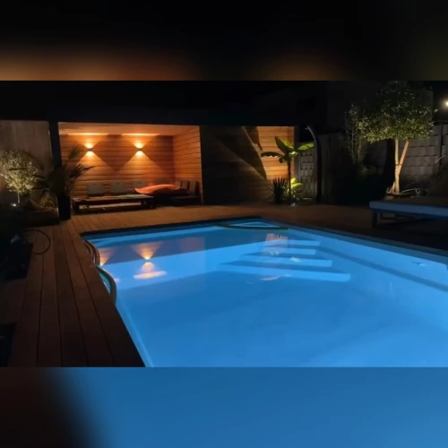 Pool house en ossature bois éclairé de nuit au bord d’une piscine à Drusenheim – BH Solutions